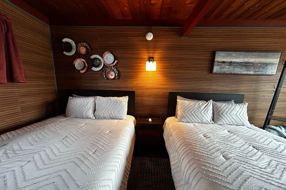 Une chambre avec deux lits, des murs lambrissés, une horloge murale, un luminaire fixé au mur et un tableau.