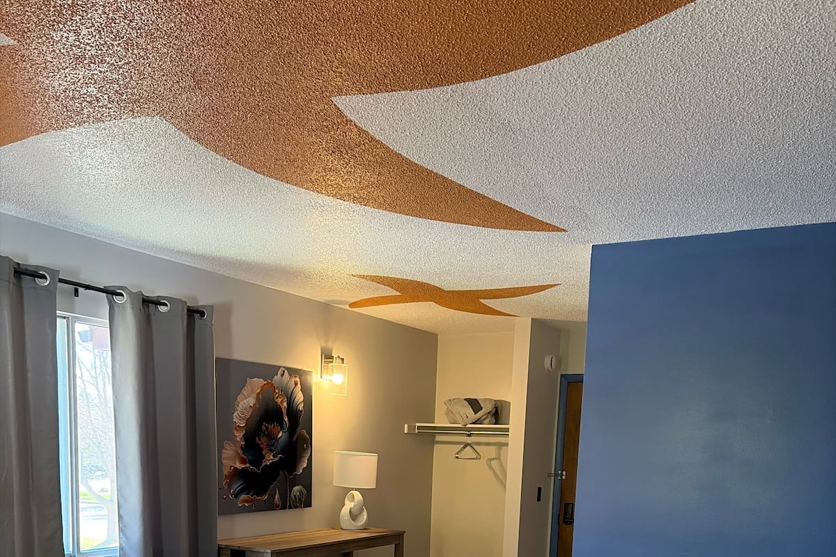 Une chambre d’hôtel avec un lit, un bureau, une chaise, une lampe et un tableau au mur.