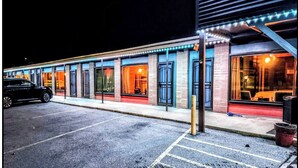 Um edifício com várias janelas e portas, um estacionamento e um veículo.