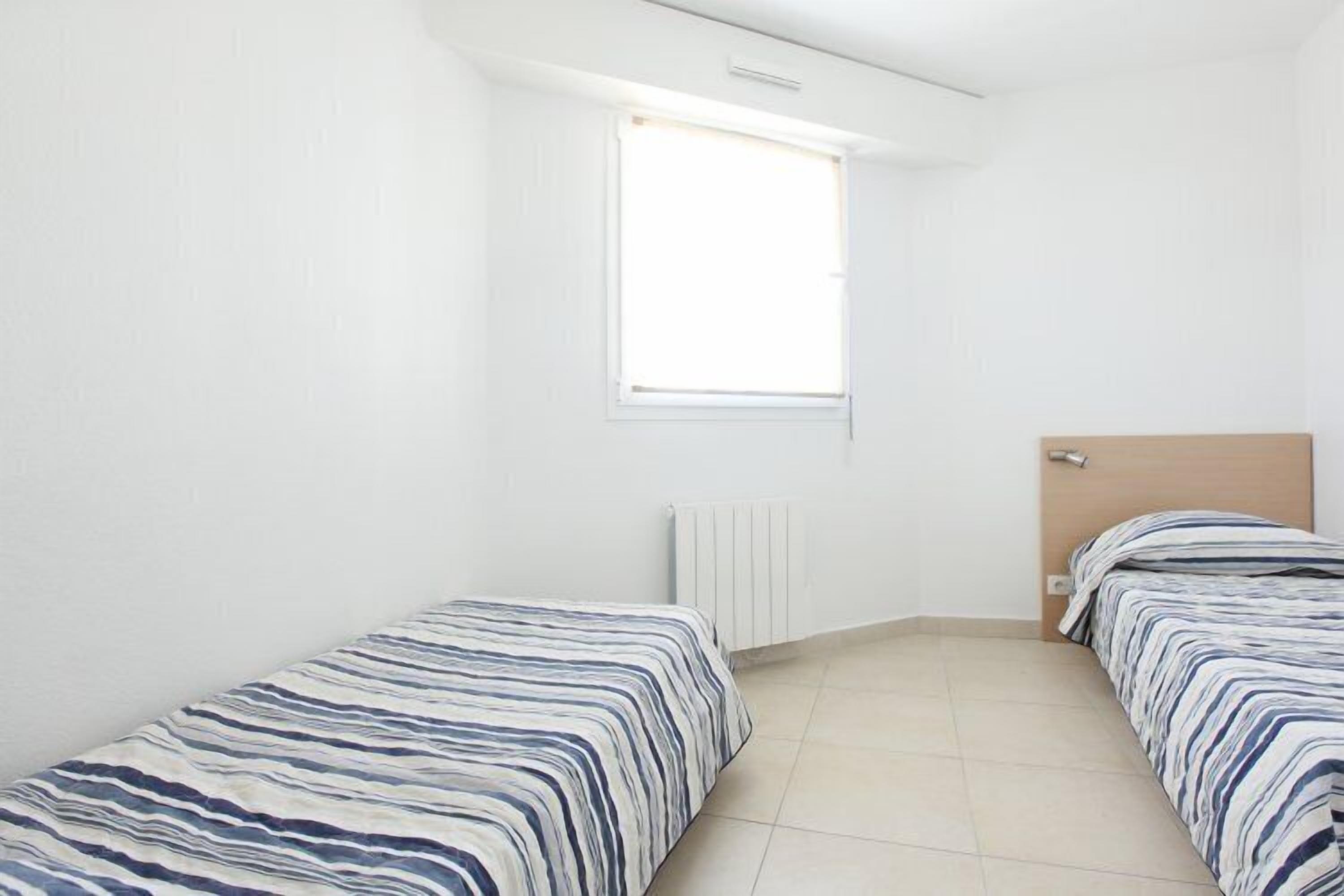 A small, clean room with two single beds, a window, and a radiator.