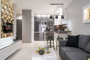 A modern living room with a grey sofa, a white coffee table, and a kitchen in the background.