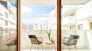 Ein Balkon mit Korbstühlen, einem kleinen Tisch mit Pflanze und Obst, und Blick auf benachbarte Gebäude.