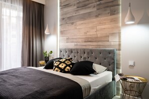 A modern bedroom with a tufted headboard, a grey bedspread, and a round side table with a magazine.