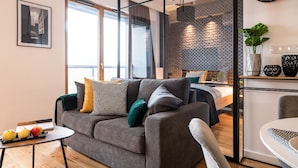 Ein modernes Wohnzimmer mit Sofa, Esstisch und sichtbarer Küchenzeile durch eine offene Tür.
