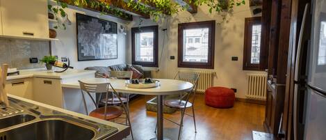 A modern kitchen with a central island, wooden beams, and hanging plants.