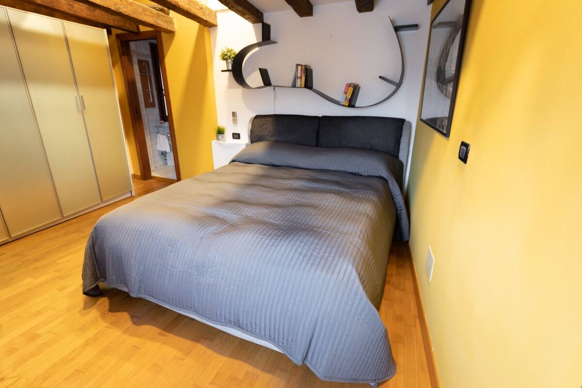 Un dormitorio con cama, suelo de madera, armario empotrado y estante curvo con libros.