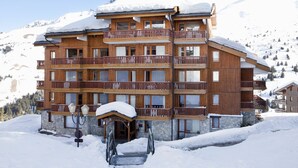 Un immeuble en bois à plusieurs étages, doté de balcons, entouré de montagnes enneigées.