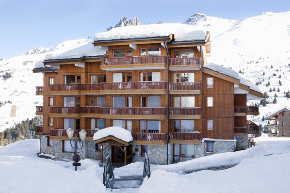 Un immeuble en bois à plusieurs étages, doté de balcons, entouré de montagnes enneigées.