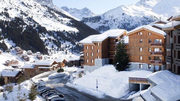 Une station de montagne enneigée, avec des bâtiments en bois, un parking et un panneau indiquant « LE FONTOY ».