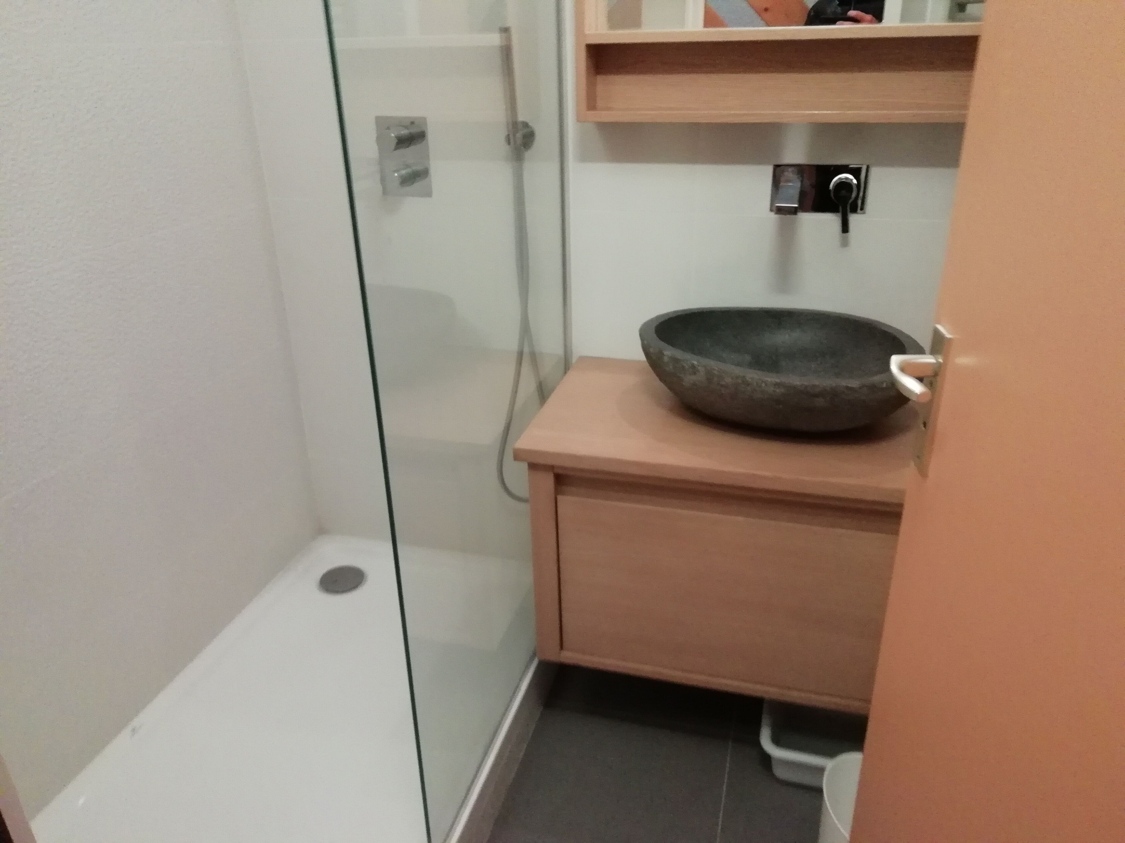 A small bathroom with a glass shower enclosure, a wooden vanity with a bowl sink, and a shelf above the sink.