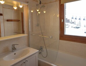 Une salle de bain avec une douche en verre, un lavabo et une fenêtre donnant sur des voitures et des immeubles en contrebas.