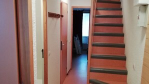 Un couloir étroit, avec une porte en bois sur la gauche et un escalier avec des rampes noires sur la droite.