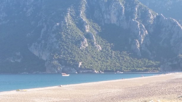A beach with a rocky cliff in the background. - Esralina Pansiyon (Kemer)