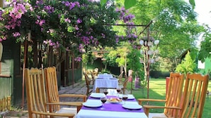 An outdoor dining area with tables and chairs, surrounded by greenery and flowering plants. - Esralina Pansiyon (Kemer)