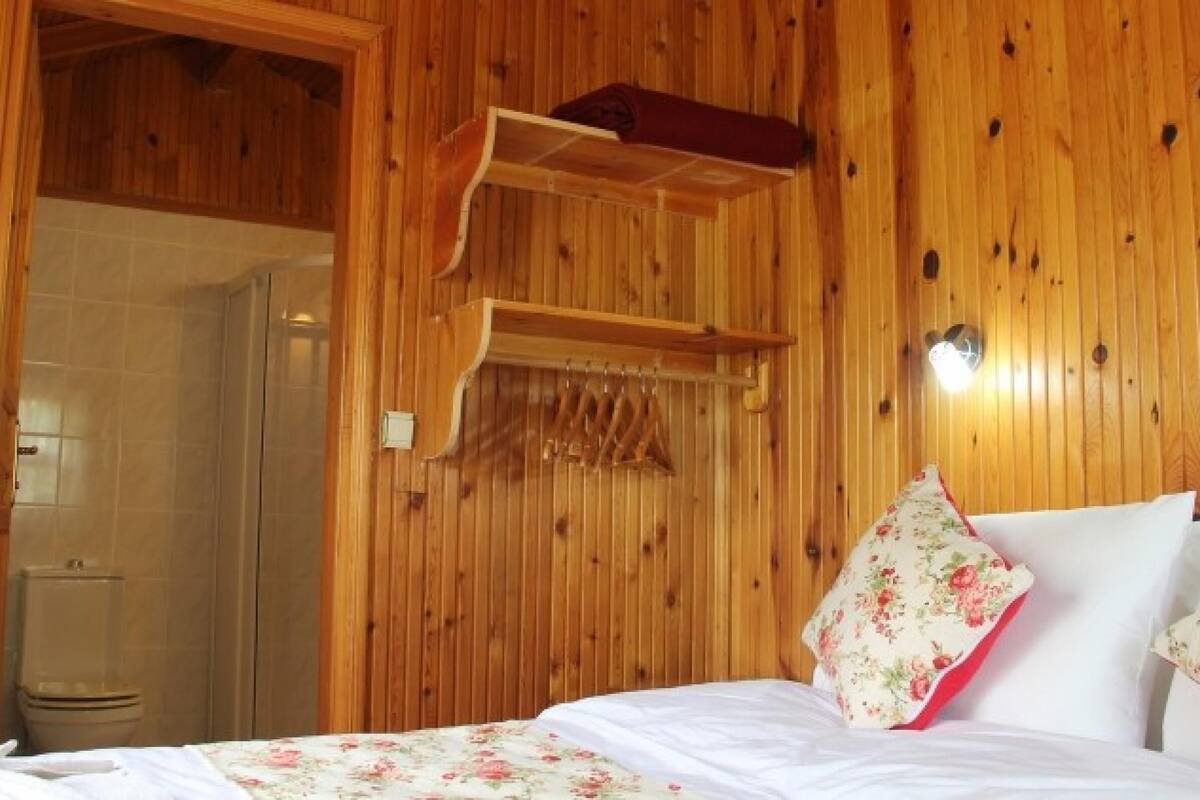A wooden room with a bed, a wooden shelf, and a shower area.