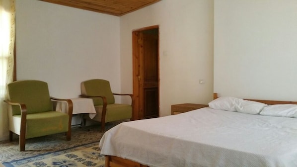 A bedroom with a bed, two chairs, a wooden door, and a small table. - Esralina Pansiyon (Kemer)