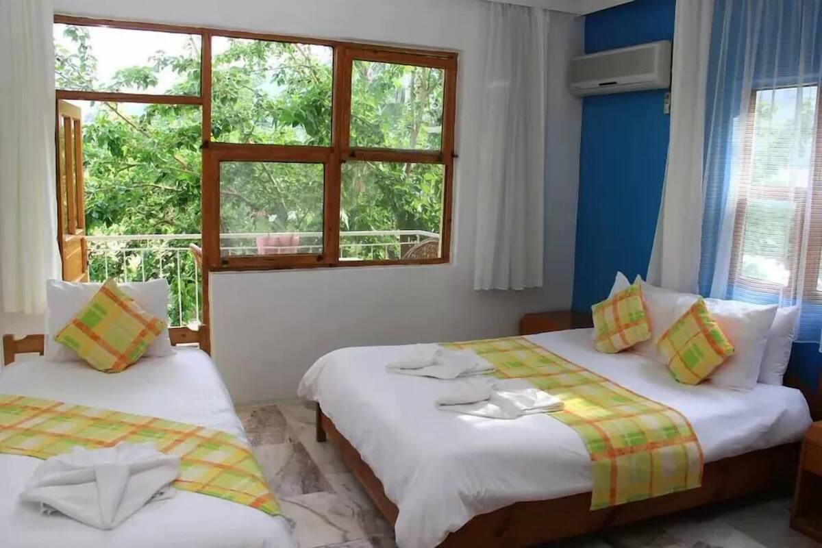 A room with two beds, a balcony, and a view of greenery.