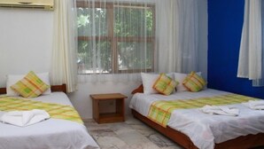 A hotel room with two beds, a small bedside table, an air conditioning unit, and a window with sheer curtains. - Esralina Pansiyon (Kemer)