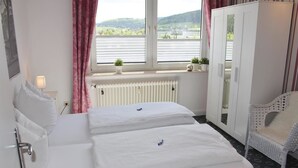 A hotel room with two beds, a radiator, a window with a view of a bridge, a wardrobe, and a chair. - Löwenstein Ferienwohnungen (Willingen)