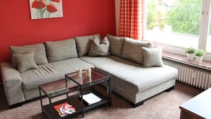 A living room with a grey sectional sofa, a glass coffee table, and a red wall. - Löwenstein Ferienwohnungen (Willingen)