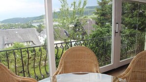 A balcony with wicker chairs and a glass table, overlooking a residential area with houses and trees. - Löwenstein Ferienwohnungen (Willingen)