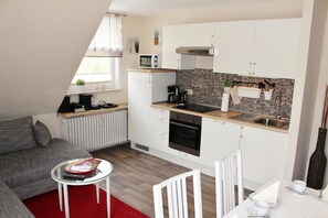 Un espace de vie compact comprenant un coin cuisine, un canapé, une petite table à manger et un tapis rouge.