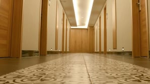 Corredor de hotel com portas de madeira, piso estampado e luminária central.