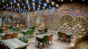 Restaurante com paredes de pedra, barris de madeira e cadeiras verdes. Mesas dispostas para refeições.
