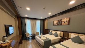 Quarto de hotel com duas camas, uma escrivaninha com cafeteira, TV e janela com cortinas.