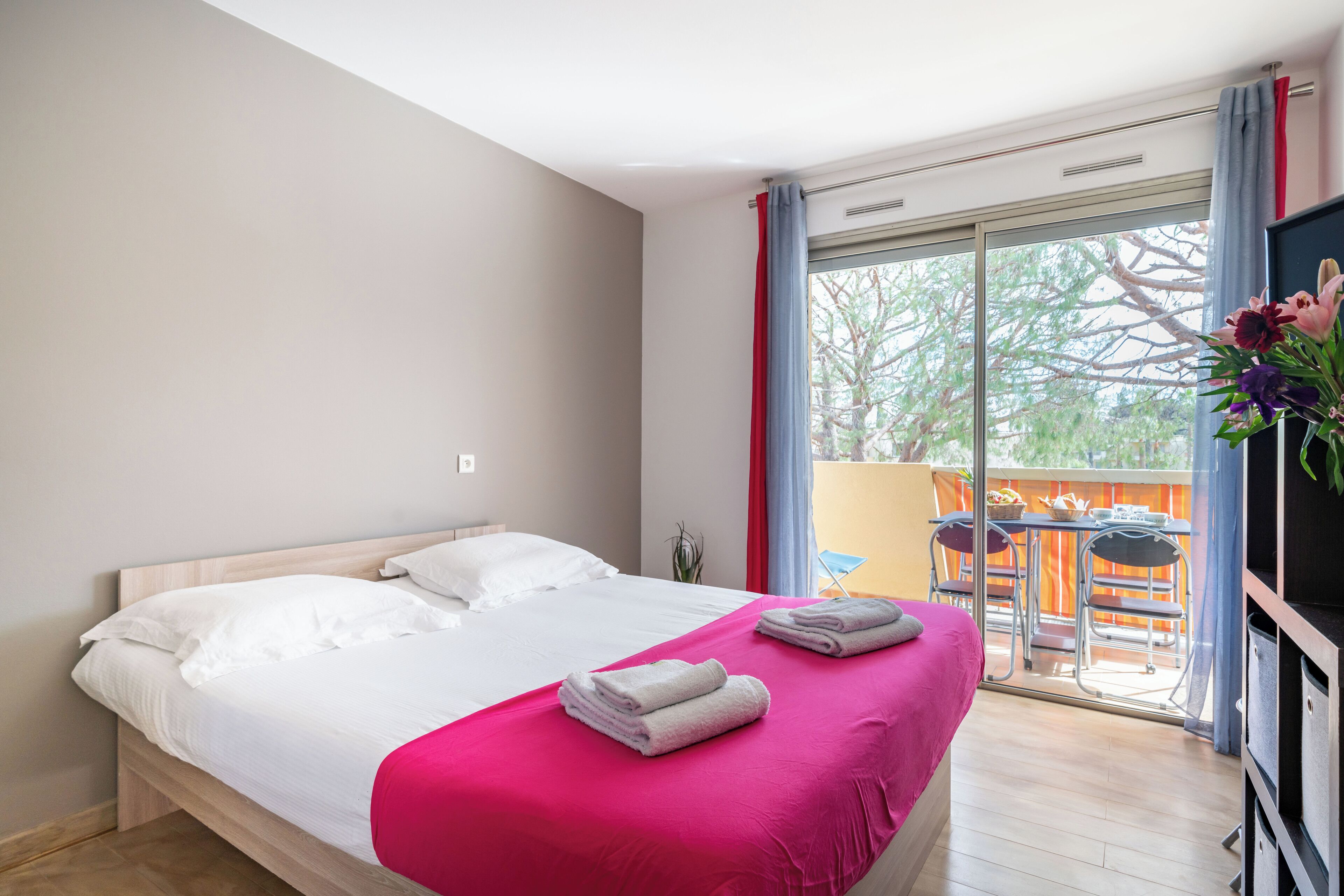 A modern hotel room with a large bed, a balcony with a table and chairs, and a TV.
