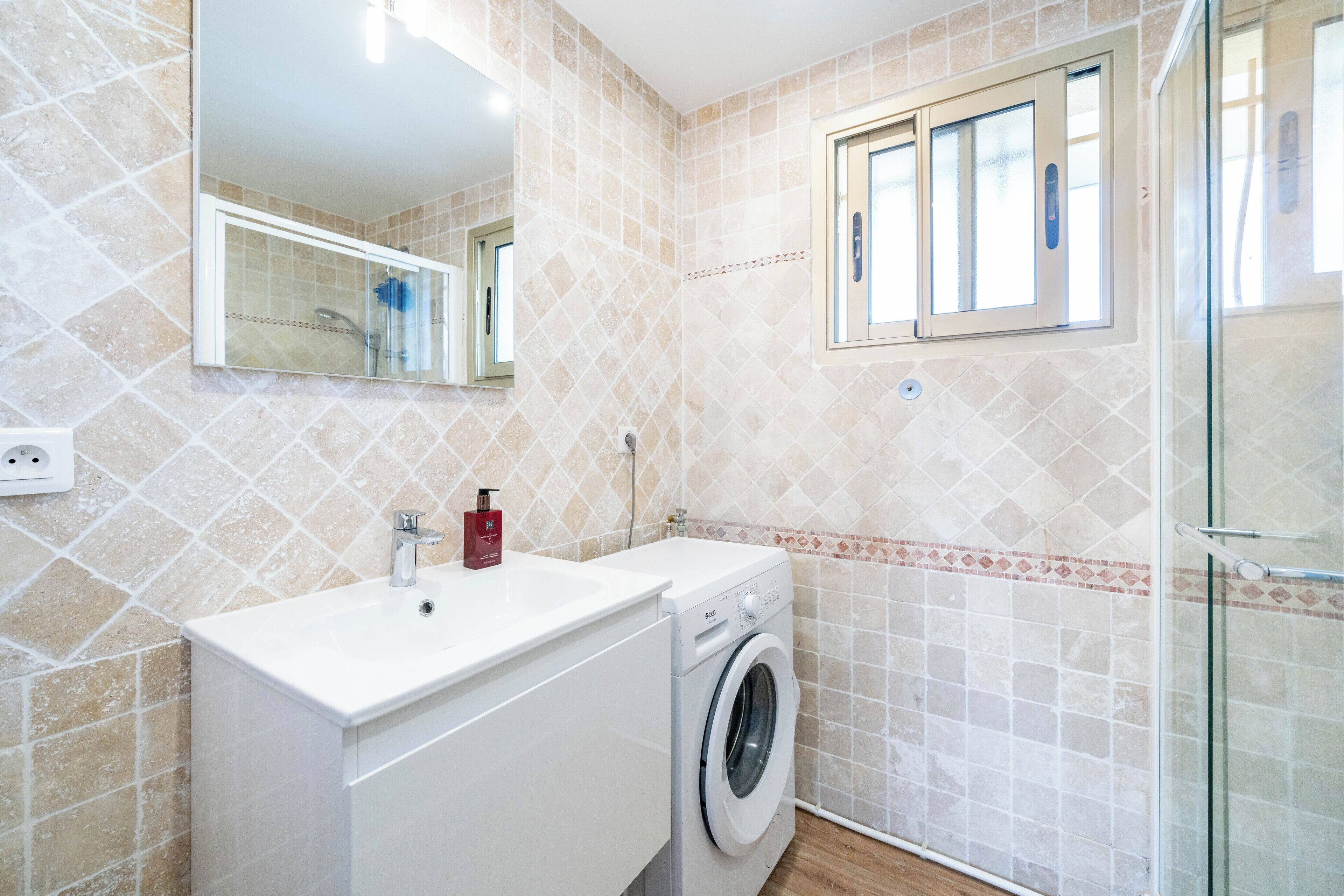 Une salle de bain moderne équipée d’un lave-linge, d’un lavabo et d’une douche à parois de verre.