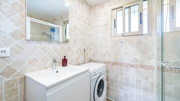 Une salle de bain moderne équipée d’un lave-linge, d’un lavabo et d’une douche à parois de verre.
