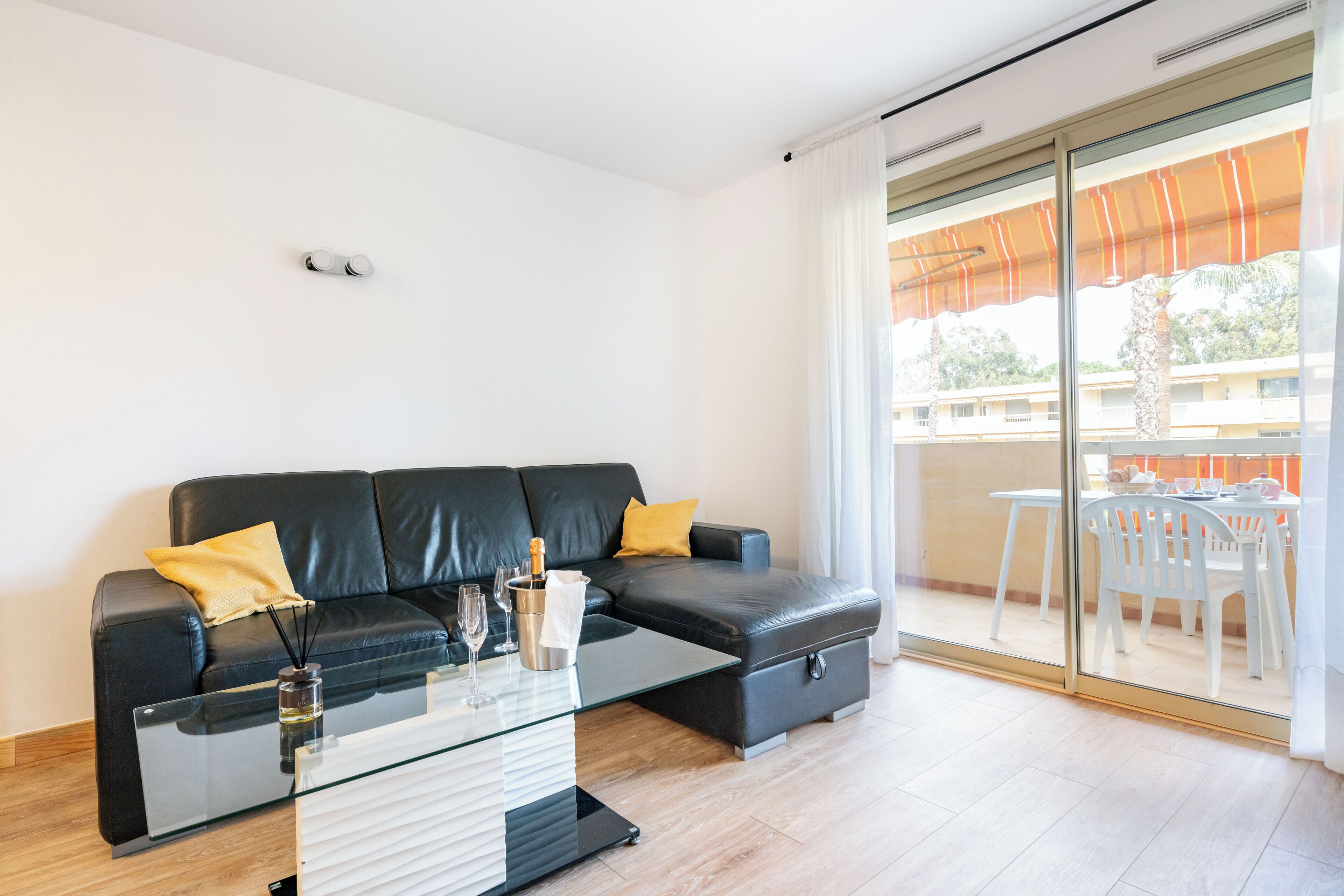 Una sala de estar moderna con un sofá de cuero negro, una mesa de centro de vidrio y un ventanal corredizo que da a un patio exterior.