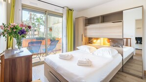 A modern hotel room with a bed, bedside tables, a desk, and a balcony with chairs. - Hello Côte d'Azur - Spacious apartments at a 5 min walk from the beach (Antibes)