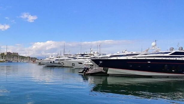 A marina with multiple yachts docked in calm waters, a clear sky, and a distant hill with buildings. - Hello Côte d'Azur - Spacious apartments at a 5 min walk from the beach (Antibes)
