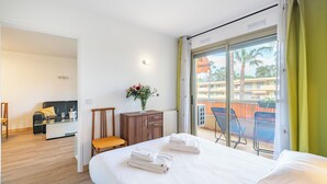 A hotel room with a bed, a bedside table, a wooden cabinet, a chair, and a view of the outside balcony. - Hello Côte d'Azur - Spacious apartments at a 5 min walk from the beach (Antibes)