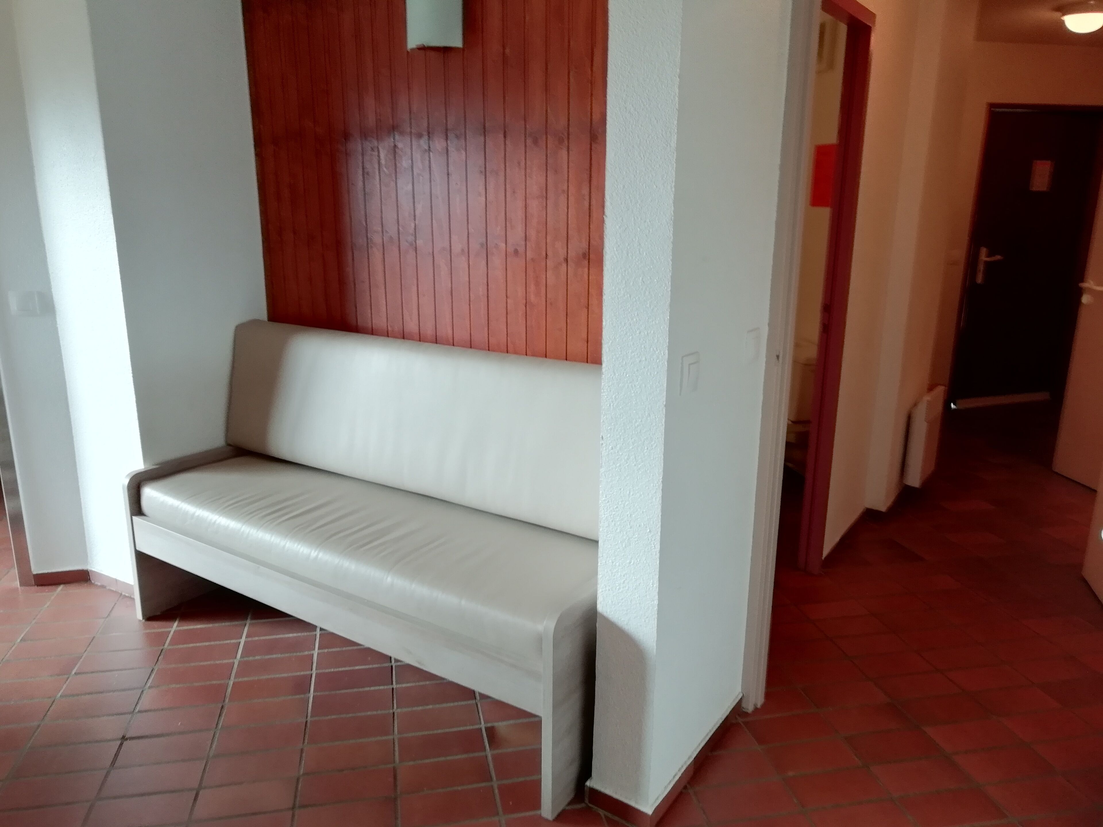Um sofá branco em um corredor com piso ladrilhado em vermelho e painéis de madeira nas paredes.