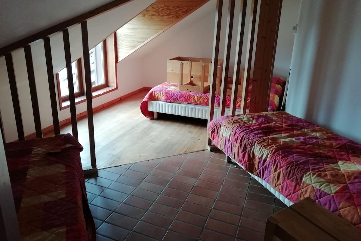 Ein Schlafraum mit zwei Betten, darunter Stockbetten aus Holz, einem Fenster und einer schrägen Decke.