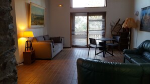 A living room with a sofa, a table with chairs, a lamp, a painting, and a window with blinds. - VVF Résidence Les Angles Pyrénées (Les Angles)