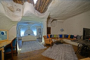 Un interior acogedor con piso de madera, un sofá con cojines de colores, una máquina de coser y una cama con cabecera blanca.