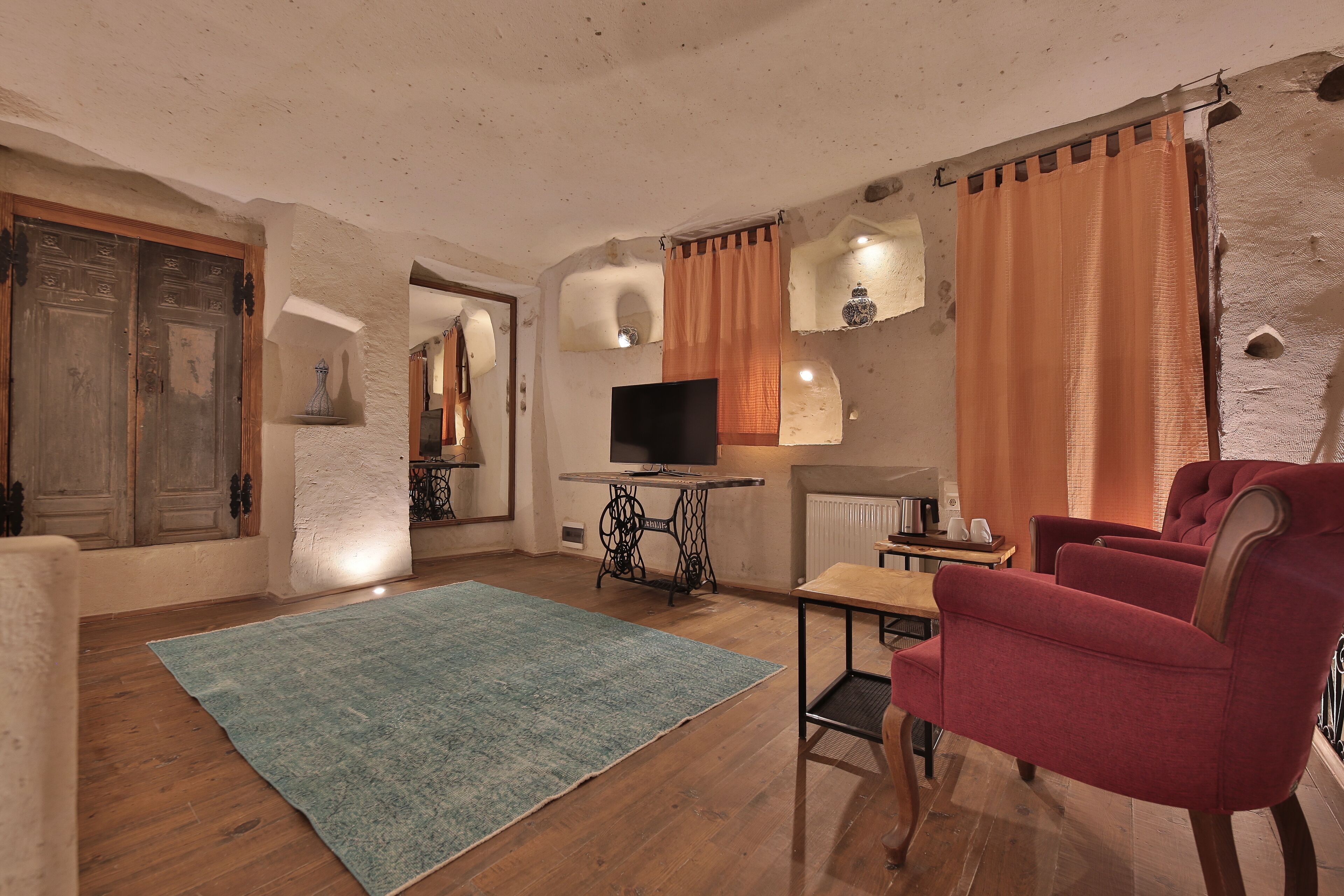 Un accogliente soggiorno con pavimento in legno, un tappeto blu, una poltrona rossa, un televisore su un tavolino vintage e un muro in pietra.