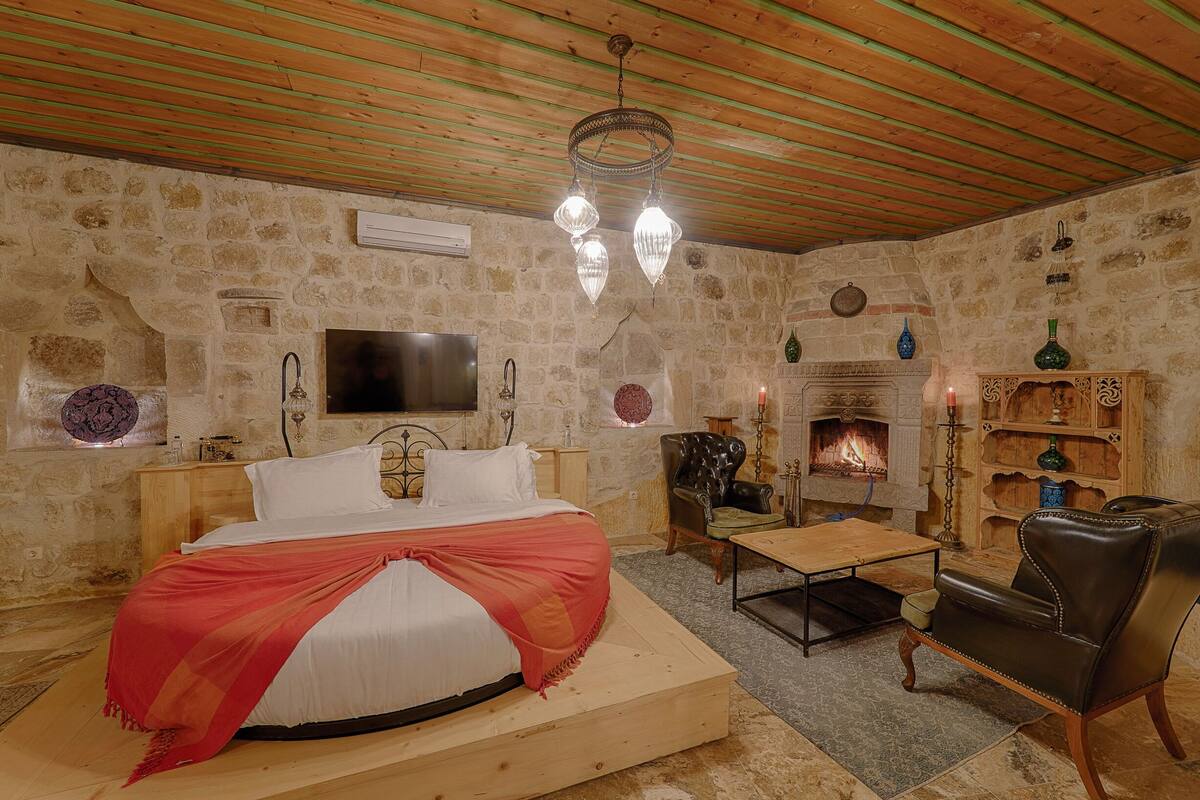 Une chambre à coucher comprenant un lit, un téléviseur, une cheminée et un fauteuil en cuir.