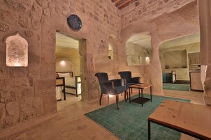 A rustic stone interior with a wooden table, two chairs, and a green rug.