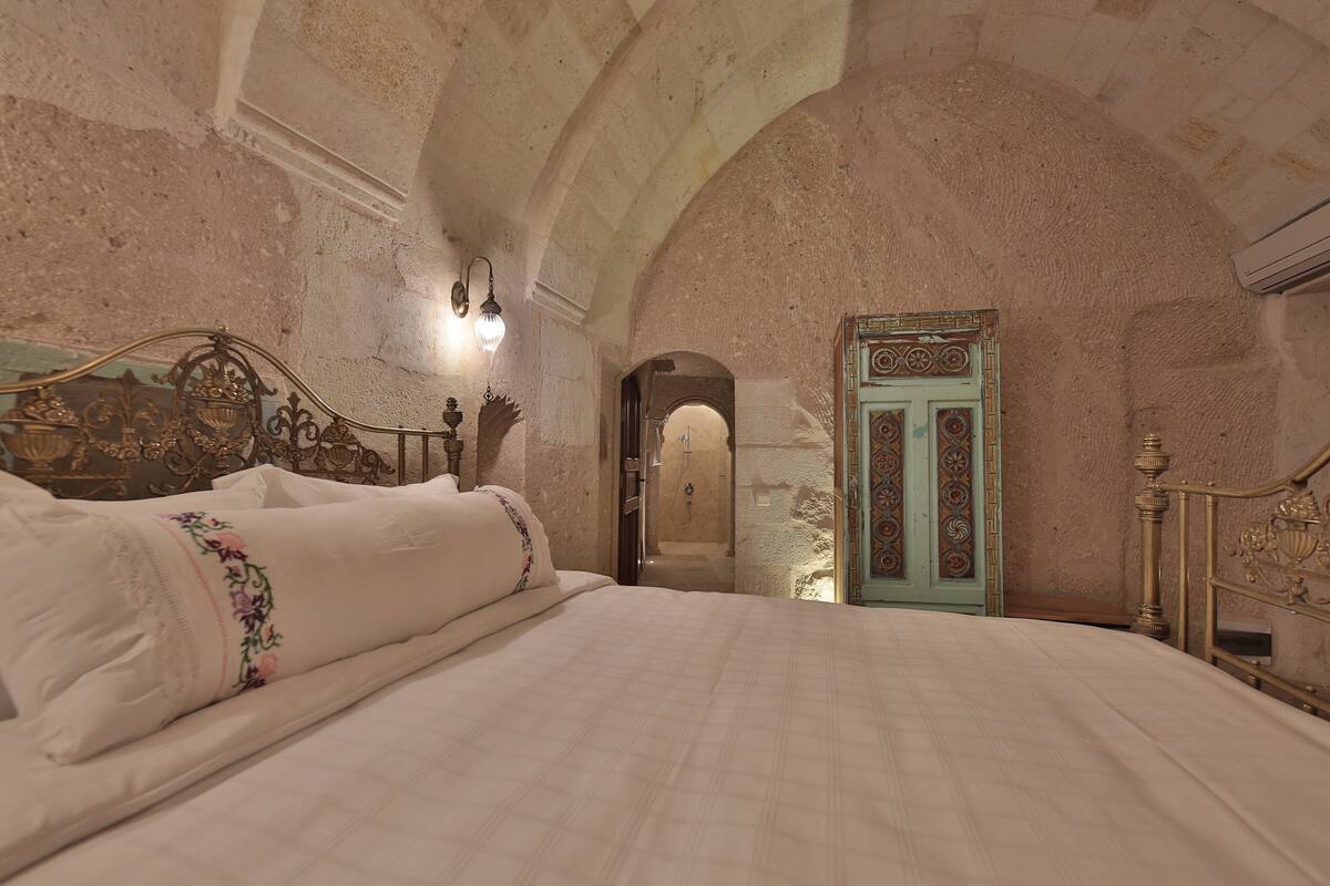 Une chambre à coucher avec un grand lit, une tête de lit en bois, un luminaire fixé au mur et une porte ornée de motifs complexes.