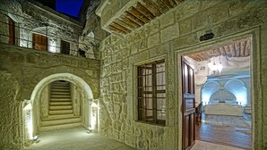 Un pasillo de paredes de piedra con una escalera que lleva a un balcón, una cama con dosel y un cartel que indica el número de habitación.