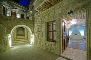 Un pasillo de paredes de piedra con una escalera que lleva a un balcón, una cama con dosel y un cartel que indica el número de habitación.