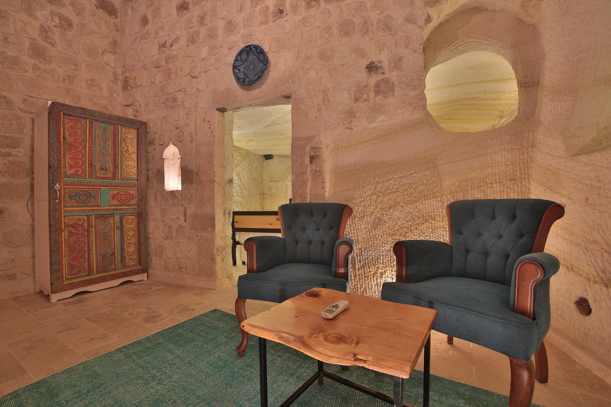 A room with stone walls, two upholstered chairs, a wooden coffee table, and a decorative cabinet.