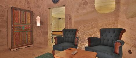 A room with stone walls, two upholstered chairs, a wooden coffee table, and a decorative cabinet.