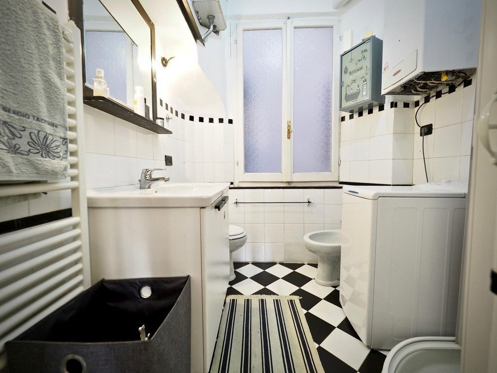 Une petite salle de bain avec un carrelage à motifs géométriques, des toilettes, un lavabo et un espace douche.