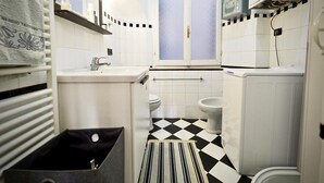 A compact bathroom with a checkered floor, a toilet, a sink, and a shower area. - Comoda Casa degli Indoratori (Genoa)